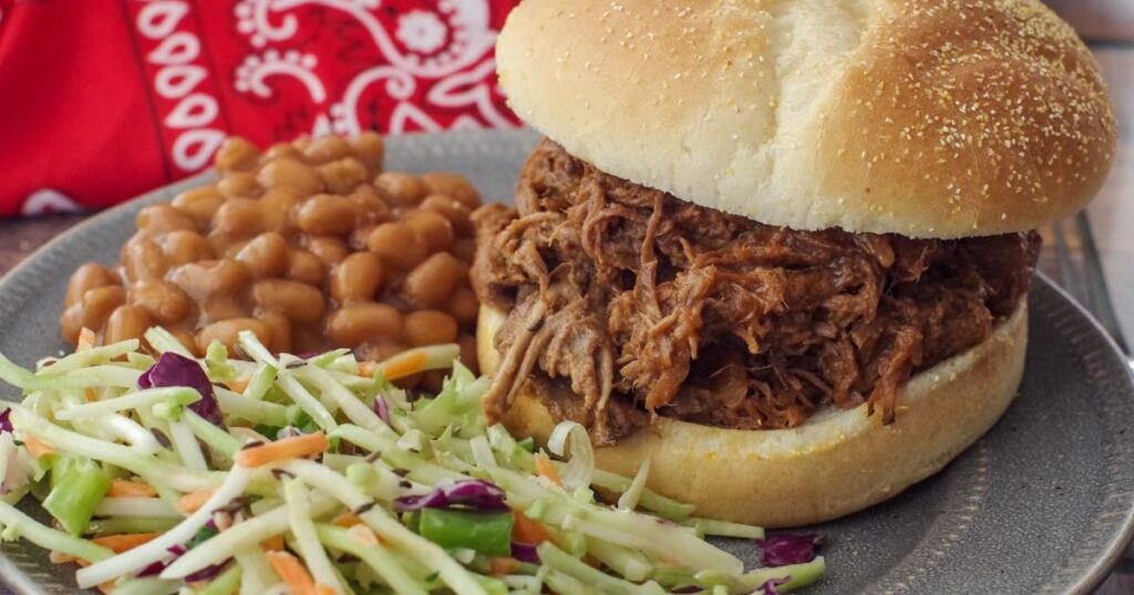 Shredded beef piled high on a bun with coleslaw and baked beans.