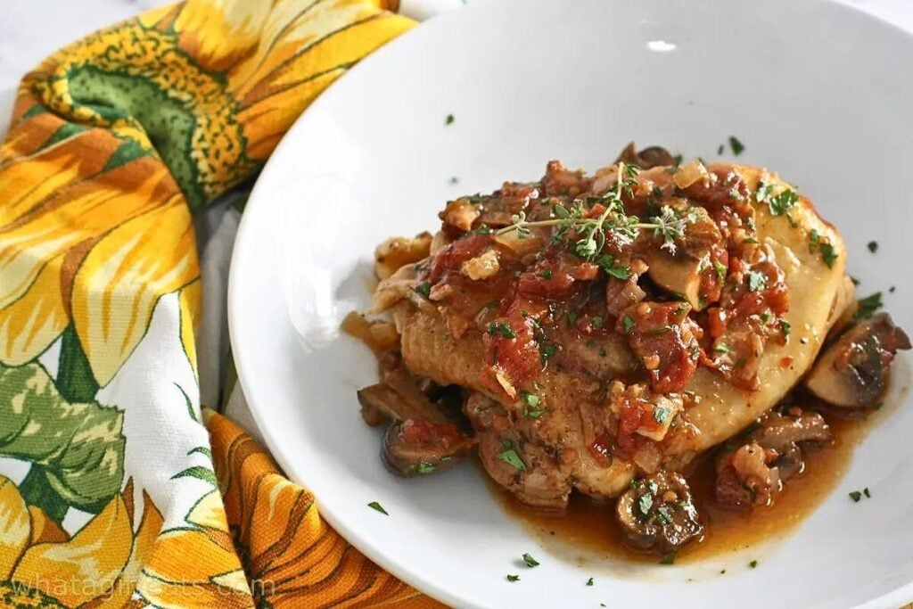 A plate of chicken with mushrooms and red sauce.