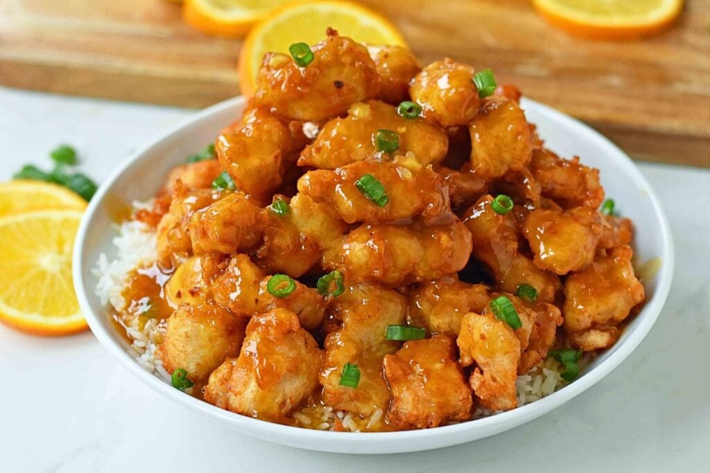 Chinese orange chicken in a bowl with green onions.