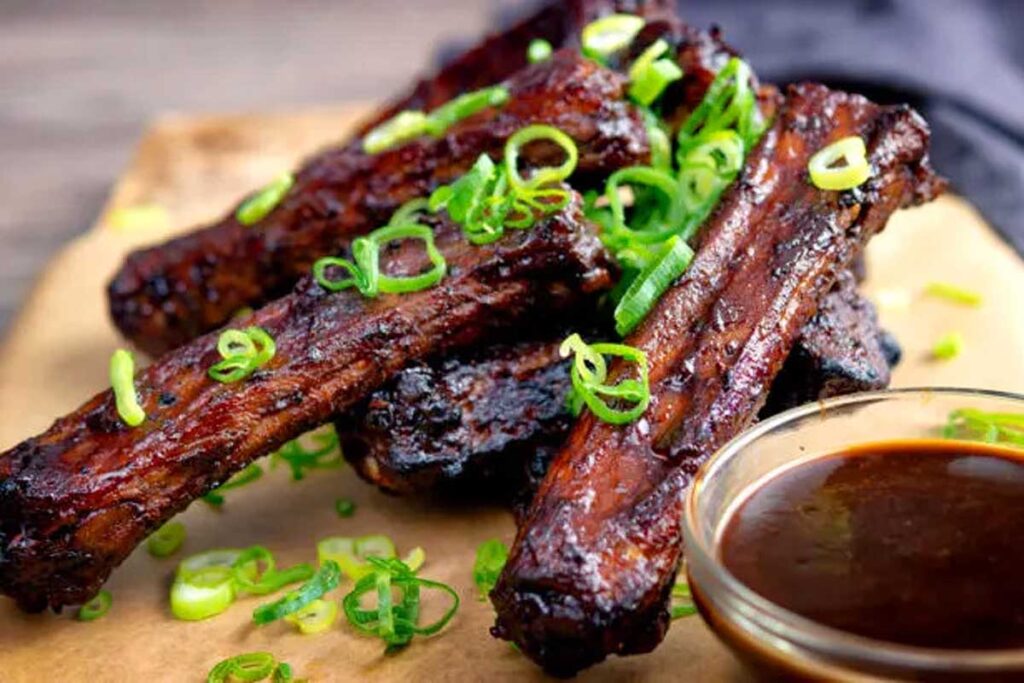 A pile of Chinese spare ribs with sauce on the side.