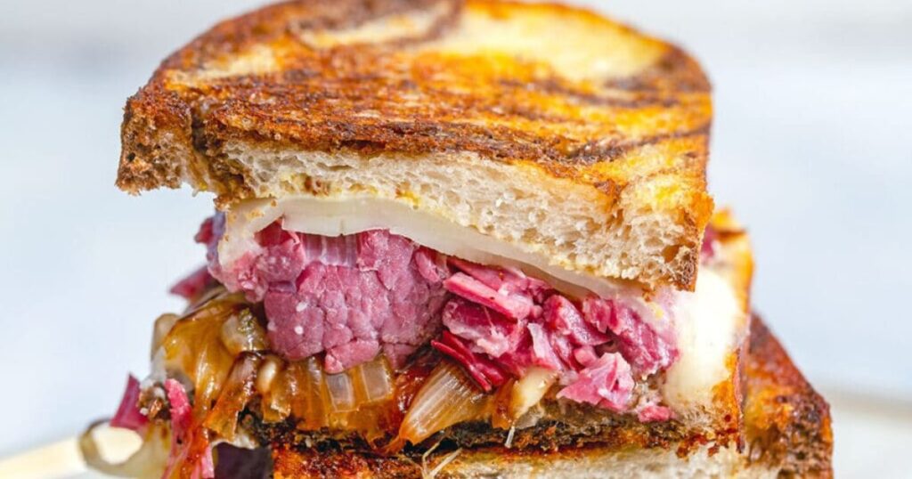A corned beef melt sandwich cut in half and stacked.