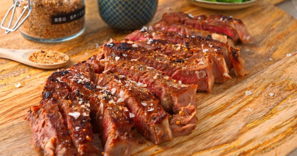 Grilled ribeye steaks sliced on a wood platter.