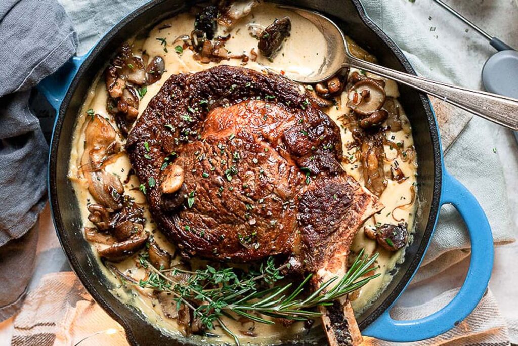 A seared steak in the pan with creamy mushroom sauce.