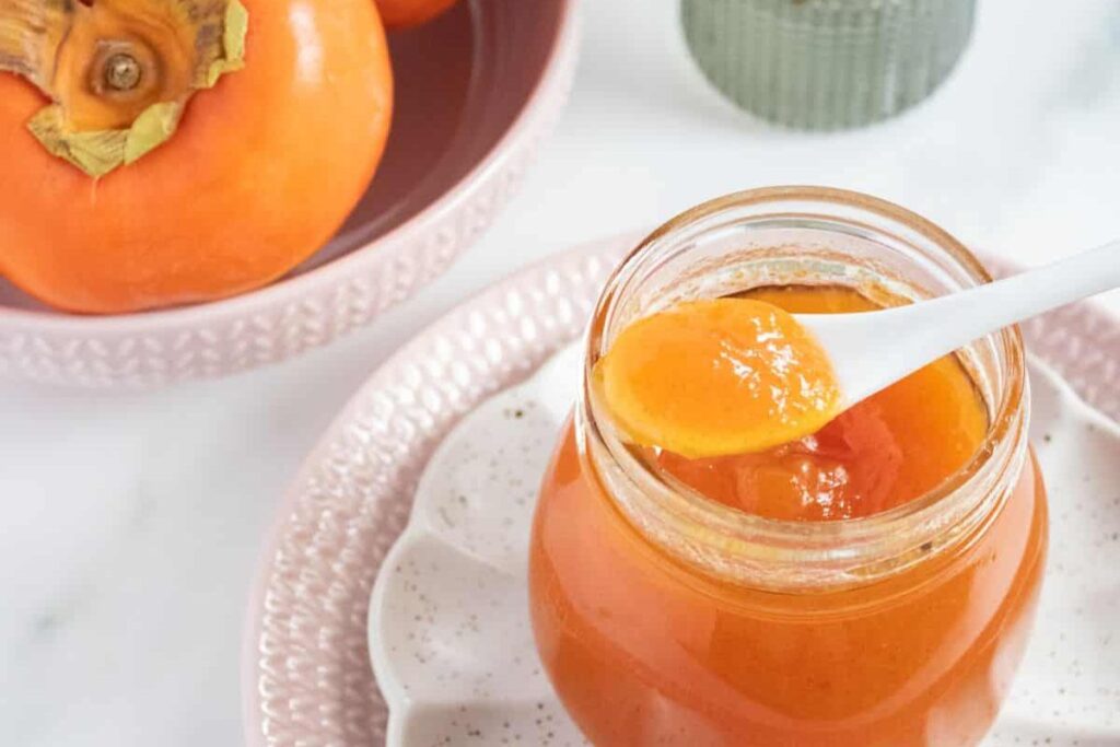 A small jar of persimmon jam on a plate.