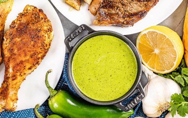 Green sauce in a black bowl with meat on the side 