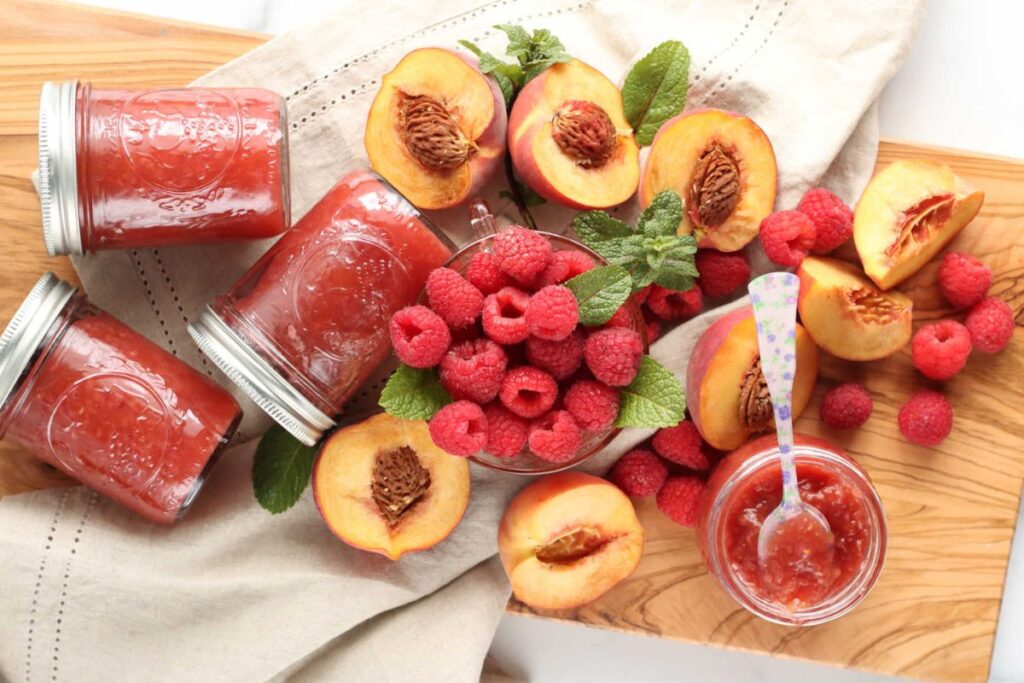 A platter of raspberries, peaches and jars of homemade jam.