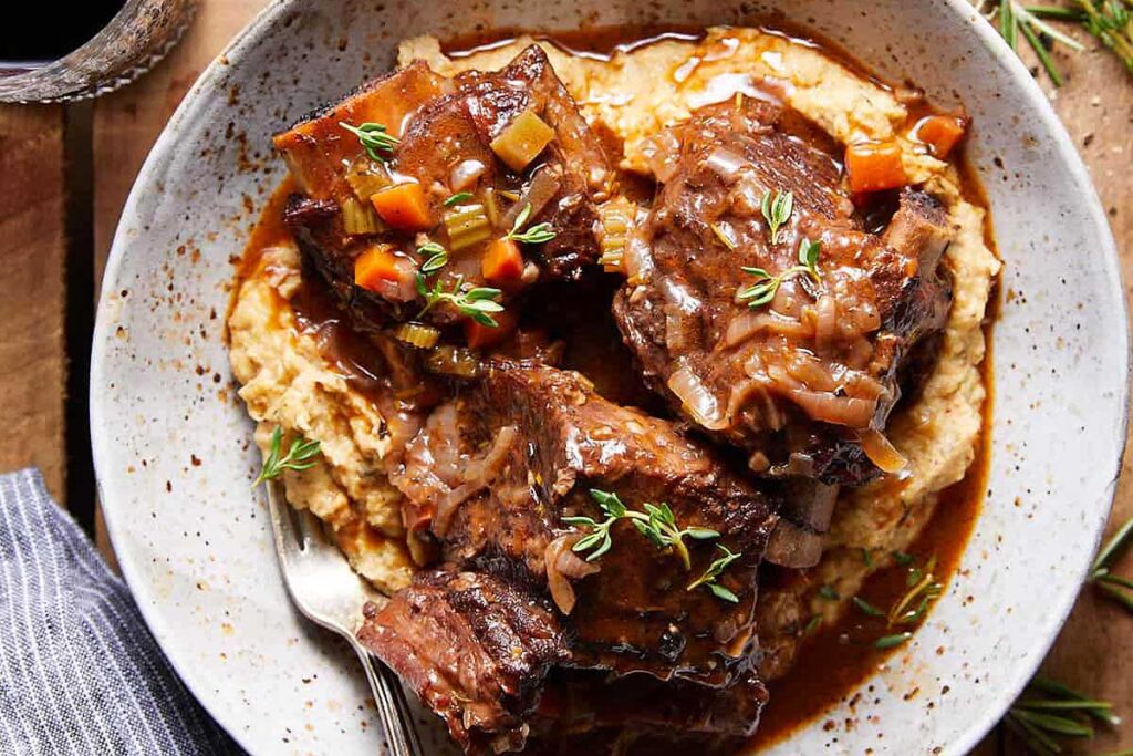A  plate of mashed potatoes topped with red wine ribs.