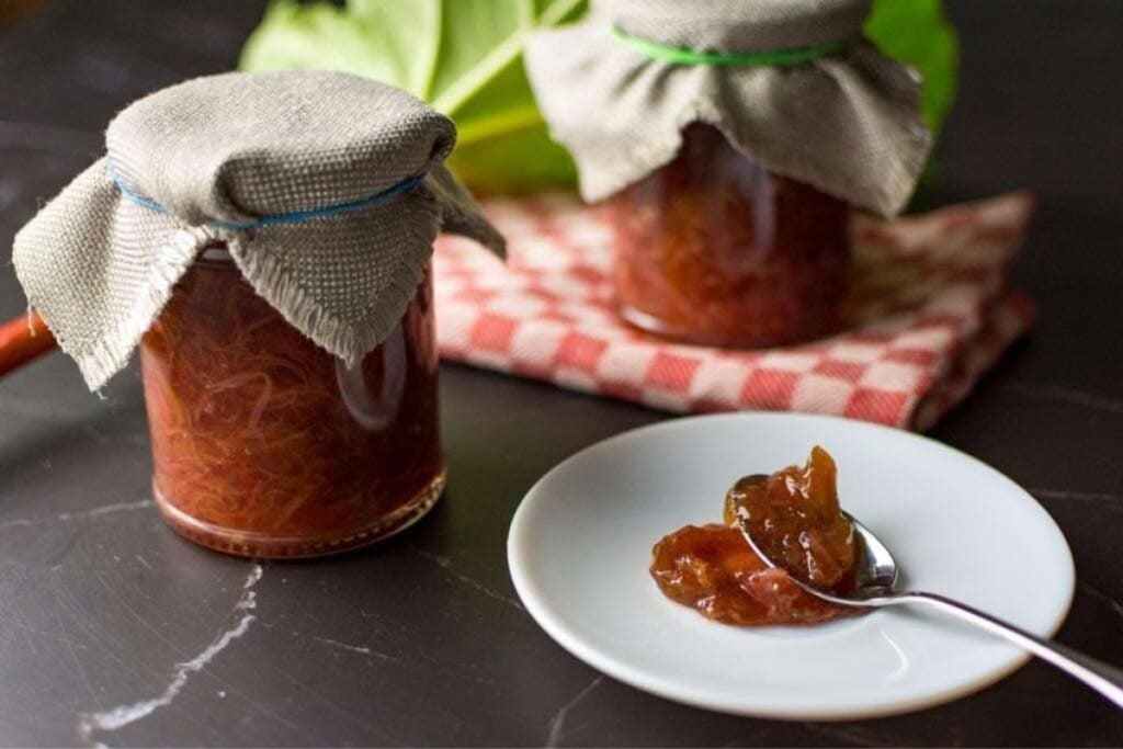 A jar of vanilla rhubarb jam with a spoonful on a plate.