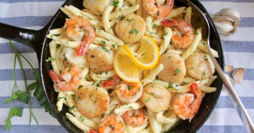 A skillet of pasta with seafood and lemons.