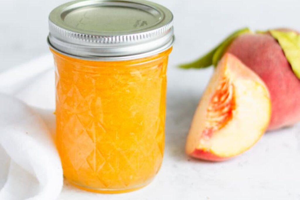 A bright colored jar of bourbon peach jam.