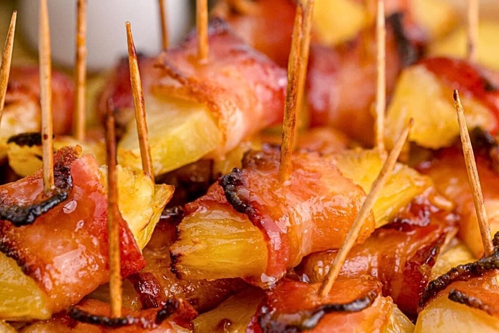 A plate of pineapple with bacon on toothpicks.