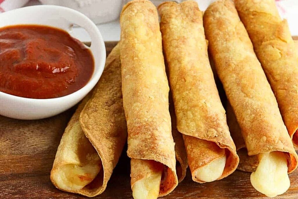 A wooden board with pizza roll ups and dipping sauce.