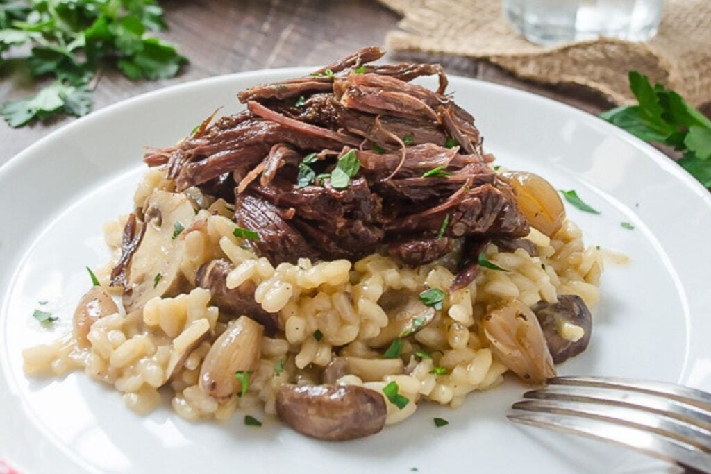 A pile of mushroom risotto with beef short ribs on top.