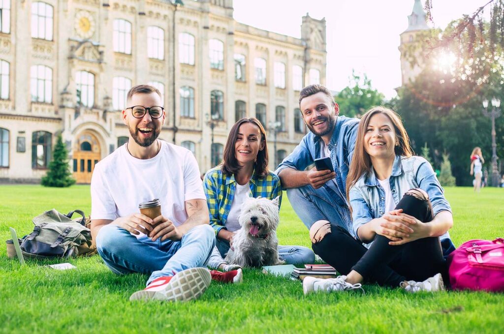 Beautiful young best friends with little funny dog on the lawn are having fun.