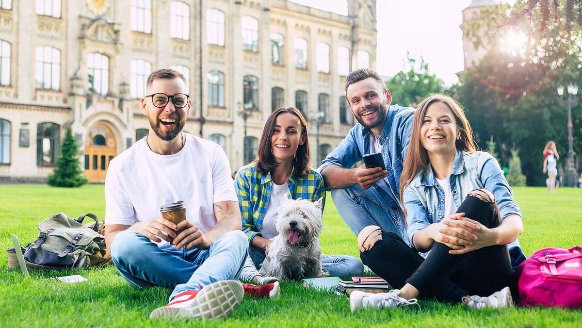 Beautiful young best friends with little funny dog on the lawn are having fun.