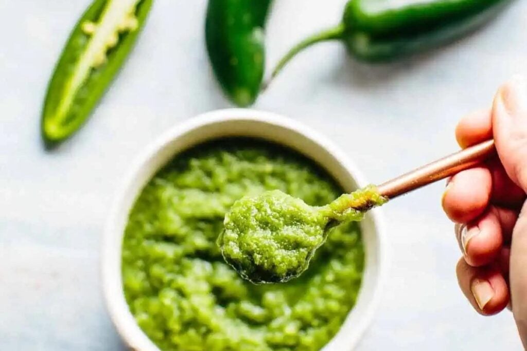 Green jalapeno hot sauce being spooned from a bowl.