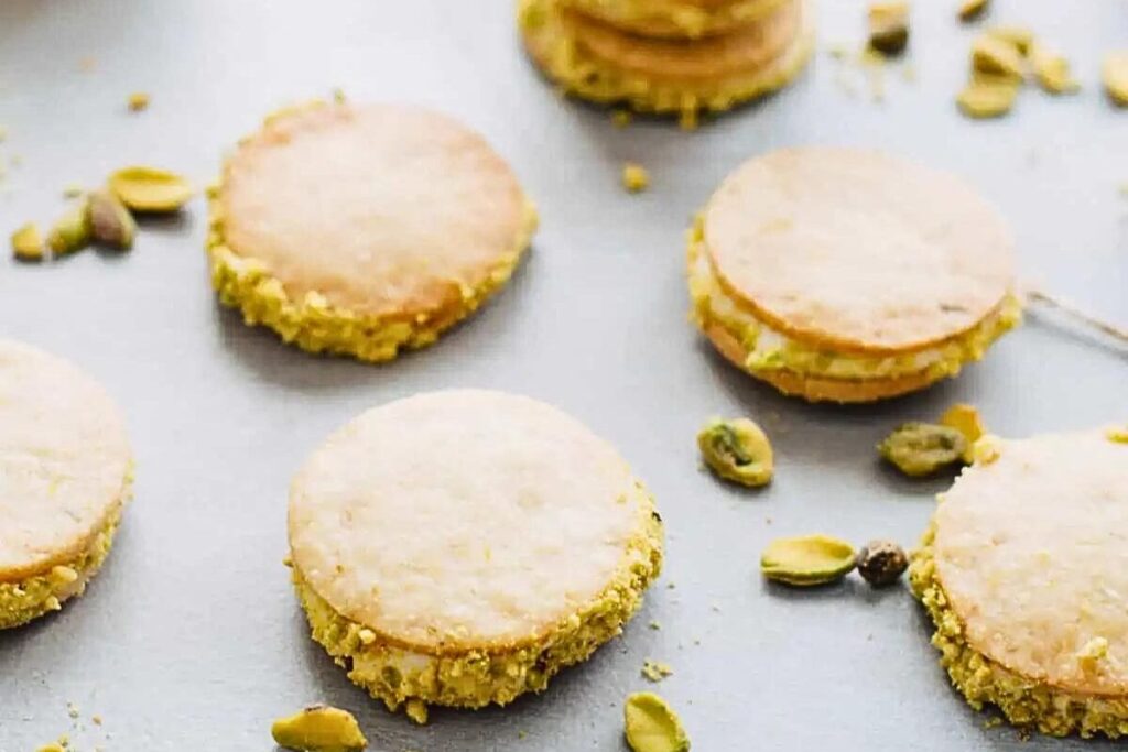 Lemon and pistachio sandwich cookies with pistachios scattered.