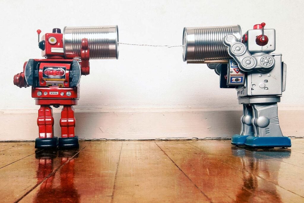 Two retro robots talk on tin can phones on an old wooden floor.