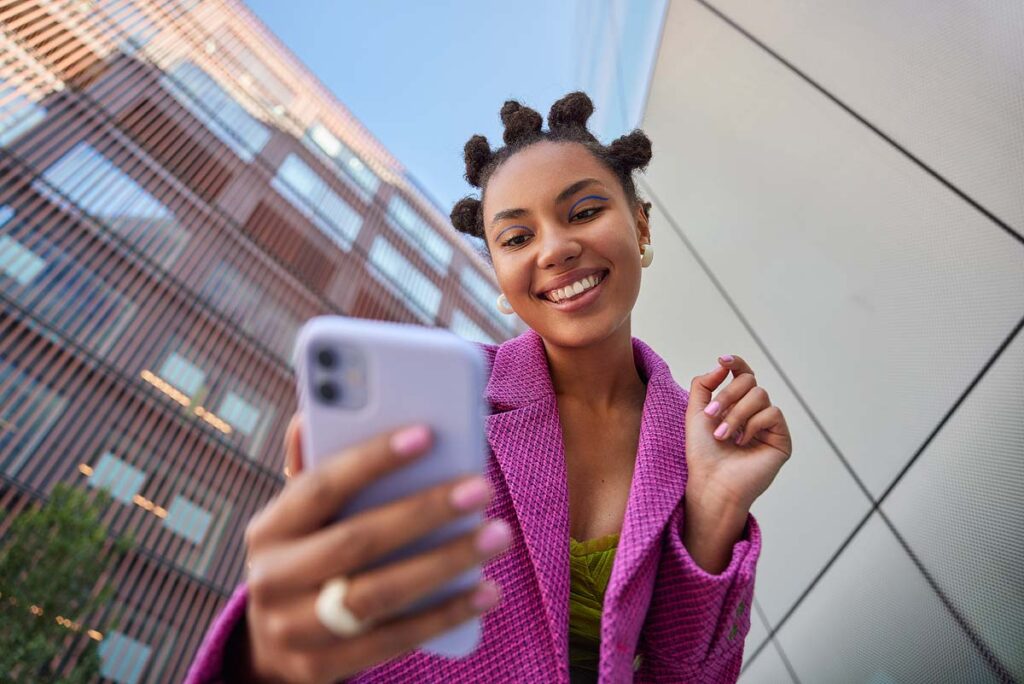 Stylish lady with hairstyle dressed in fashionable pink jacket takes selfie on mobile phone.