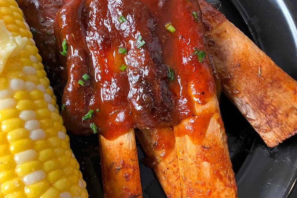 Riblets with sauce on a plate with corn.