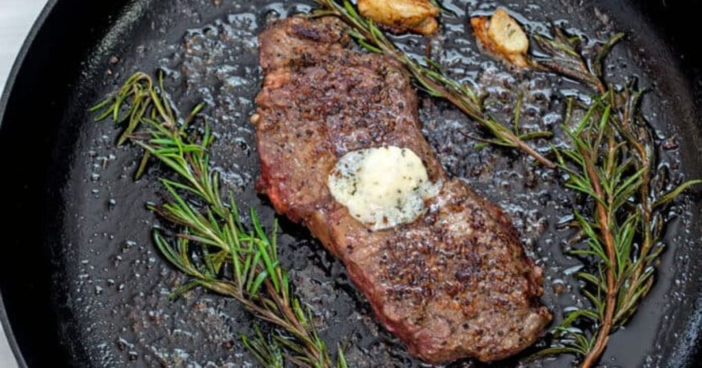 A steak in a skillet with butter and rosemary.