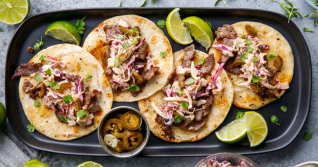 A plate of street tacos with limes and jalapenos.