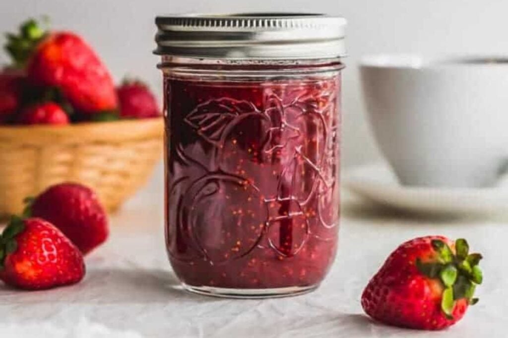 A jar of strawberry earl grey jam with fresh berries around.