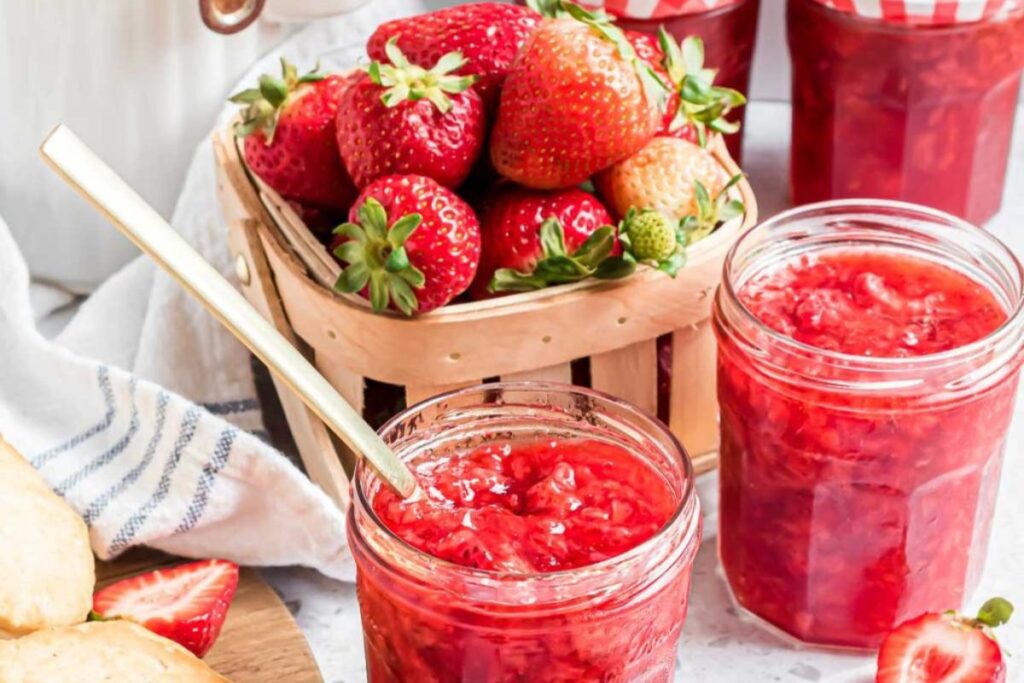 Jars of strawberry jam with fresh berries around.