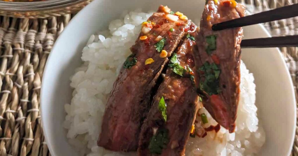A bowl of rice with strips of Thai crying tiger steak on top.