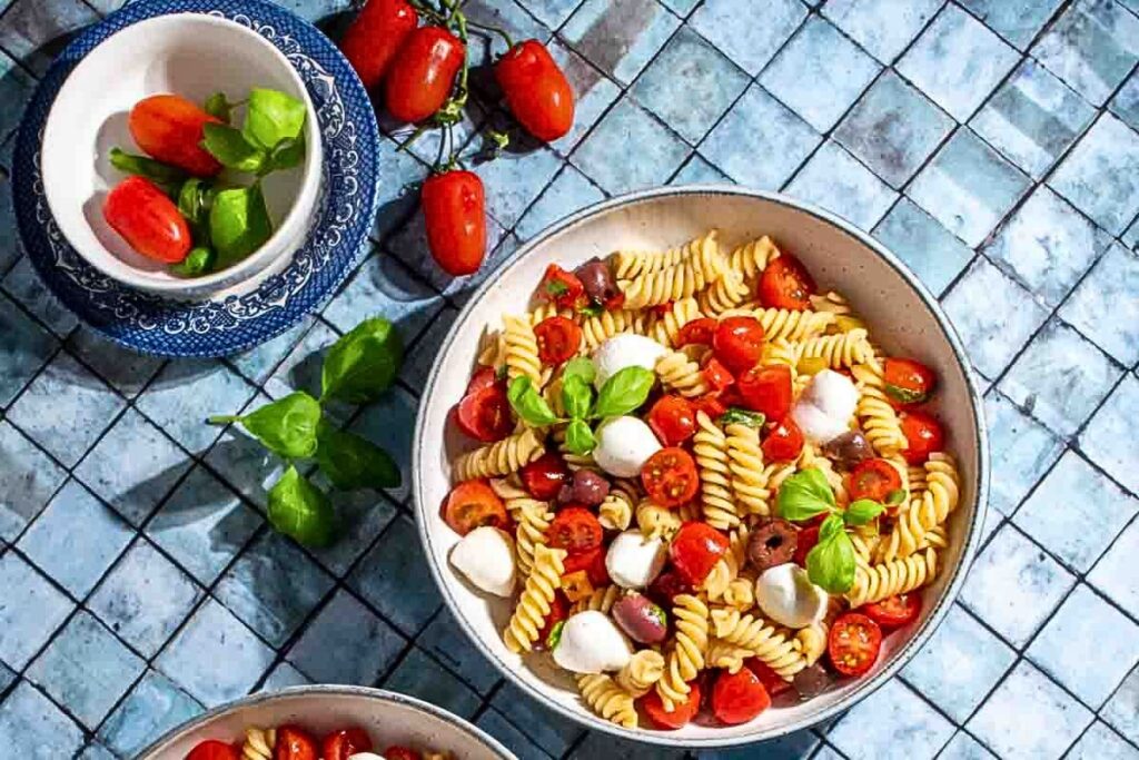 Bowls of pasta fredda with olives, cheese and tomatoes.