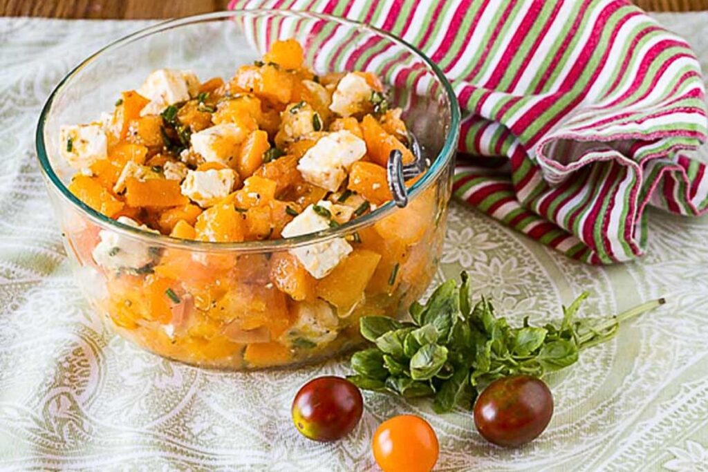 A bowl of salad made with yellow tomatoes and basil, with feta