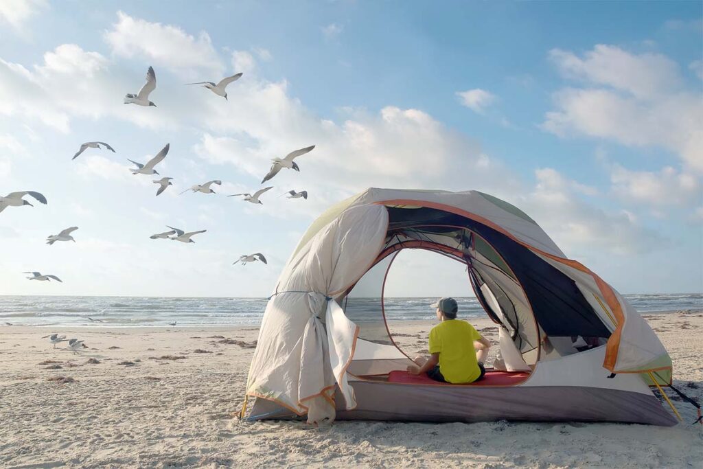 A teenager in a tent on the shores of the Gulf of Mexico looks at flying seagulls. Padre Island National Seashore, Texas, United States.