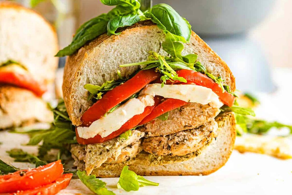 A chicken sandwich with tomato, cheese and basil.