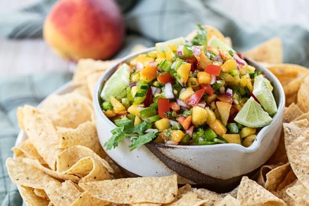 A bowl of spicy peach salsa surrounded by chips.