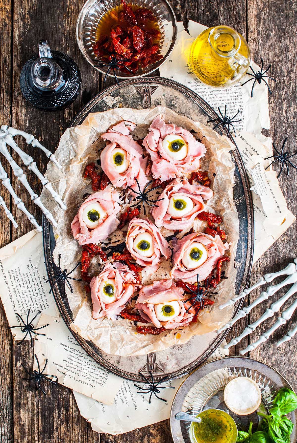 A spooky Halloween Antipasto Eyeballs Appetizer featuring ham and cheese shaped like eyeballs, surrounded by fake spiders on a rustic table.
