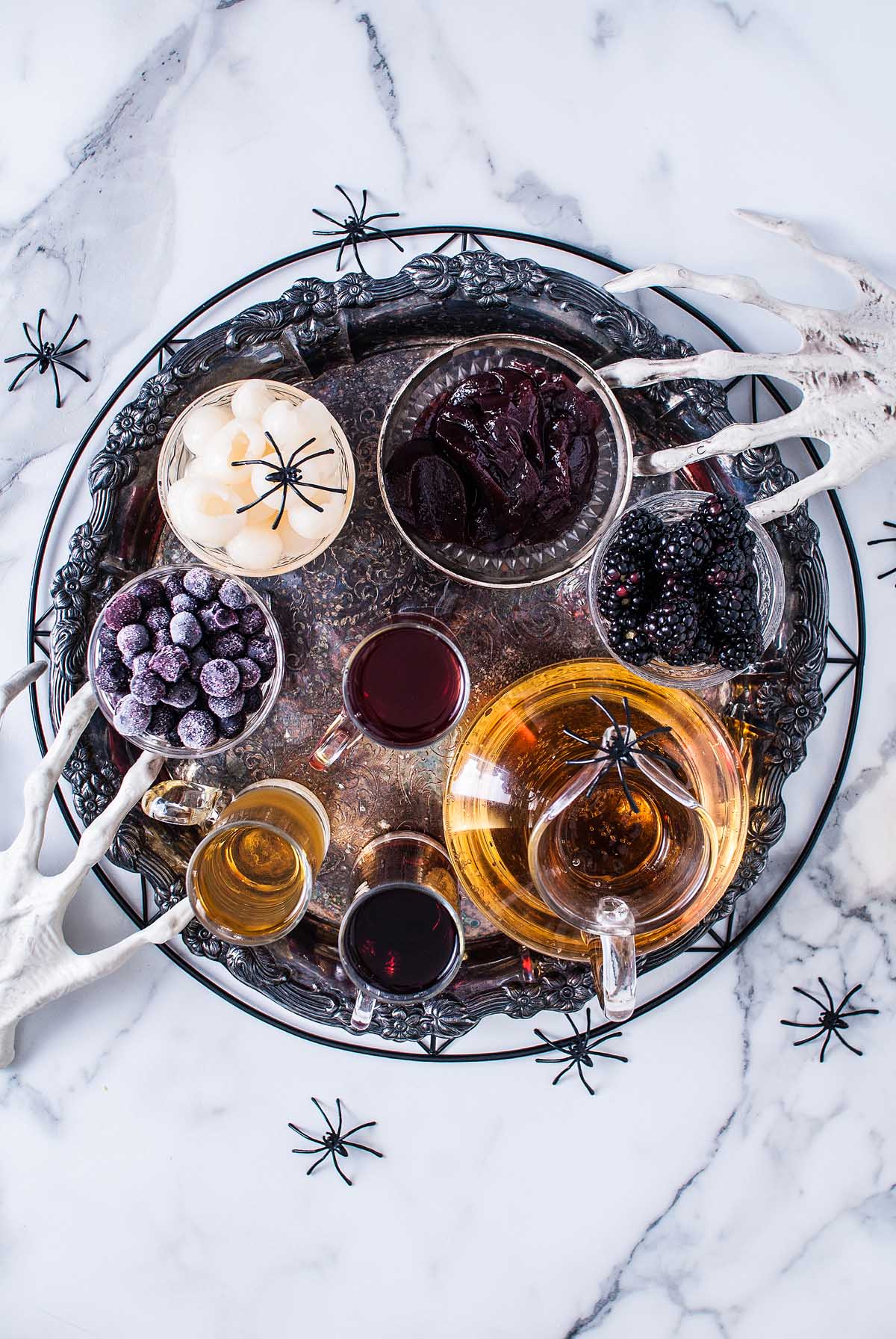 Silver tray with drinks, berries, candies, and Halloween eyeball punch, all decorated with plastic spiders and skeleton hand props for a spooky celebration.
