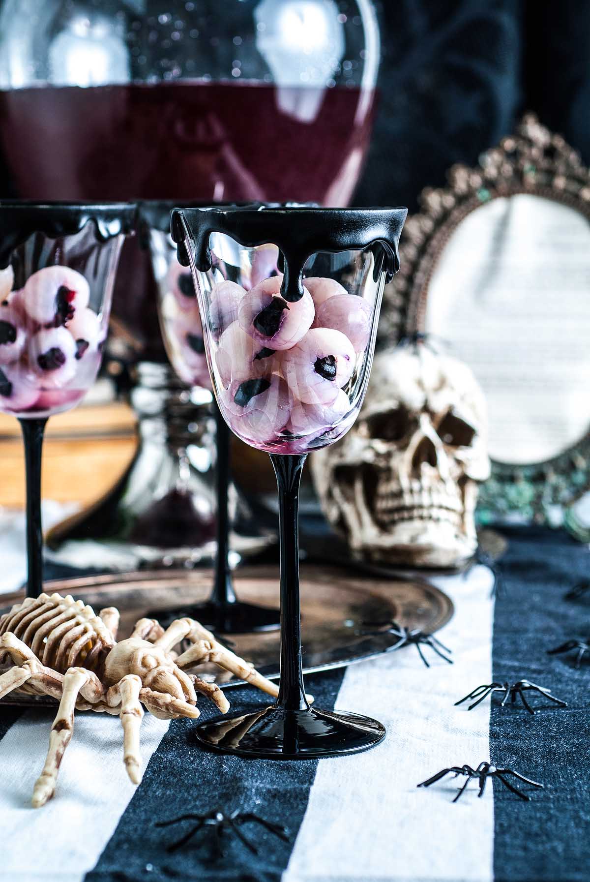 A black goblet filled with Halloween eyeball punch sits on a spooky table adorned with a skull, spiders, and eerie eyeball-like candies.