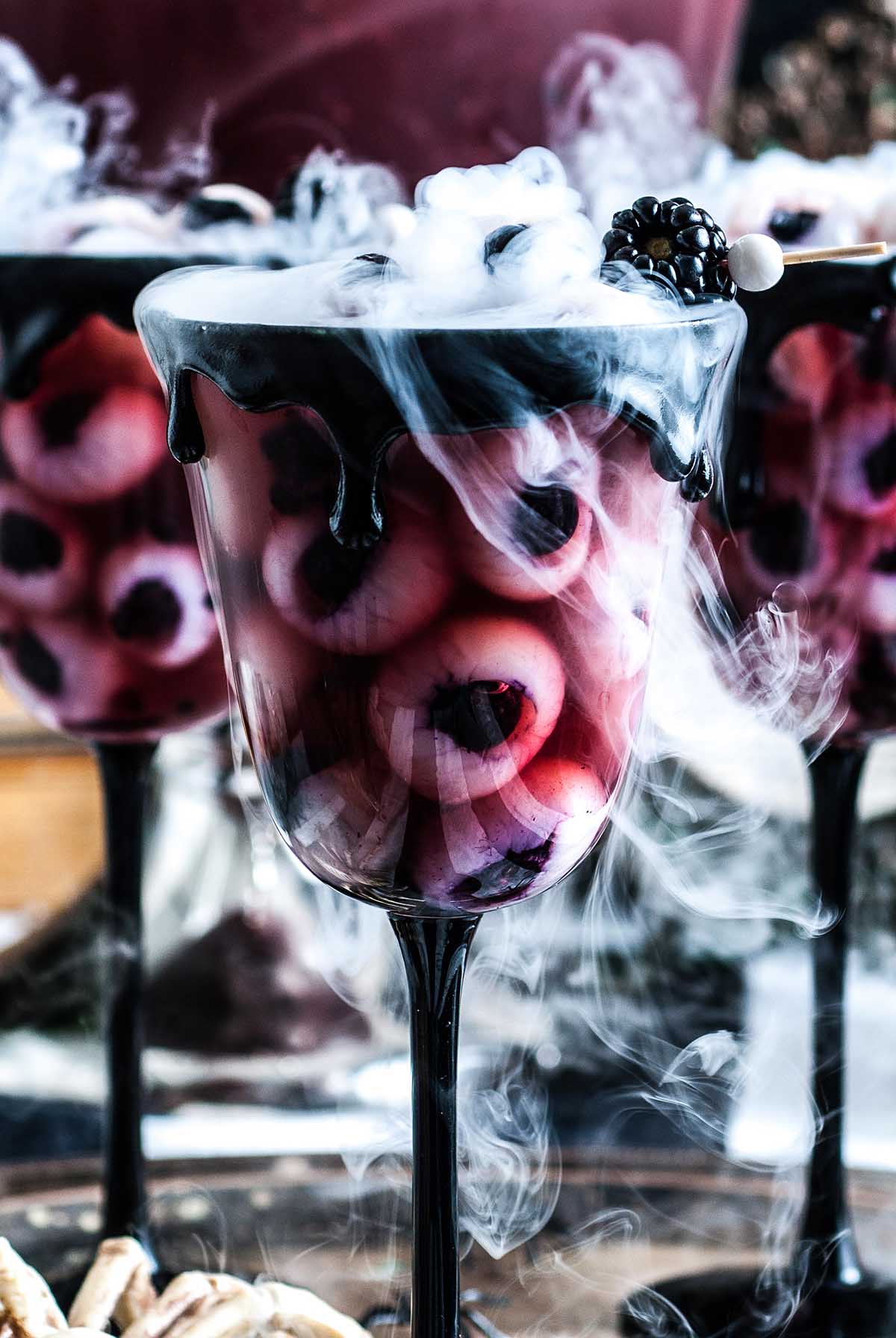 A glass filled with a Halloween drink with eyeballs and smoke from dry ice.