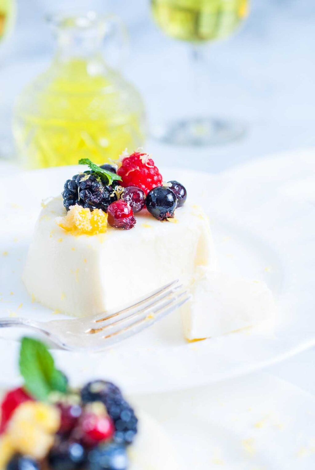 Panna cotta, a creamy white dessert topped with fresh berries and mint, served on a white plate with a fork.