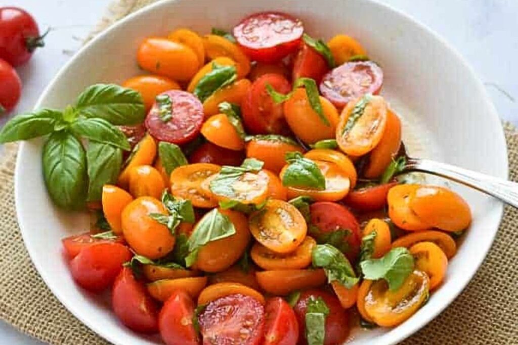 A bowl of sliced small tomatoes with basil and dressing.