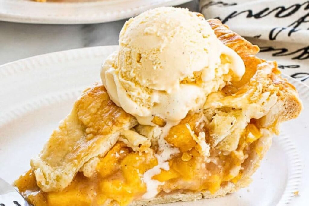 A slice of peach pie with ice cream on top.