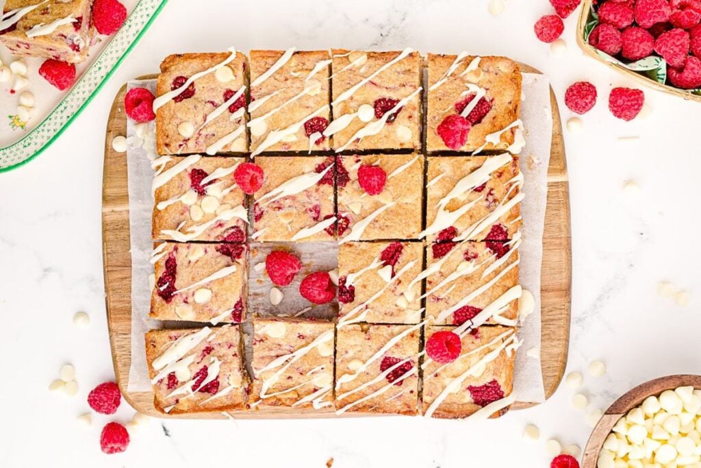 A pan of white chocolate raspberry blondies cut into squares, with fresh berries around.