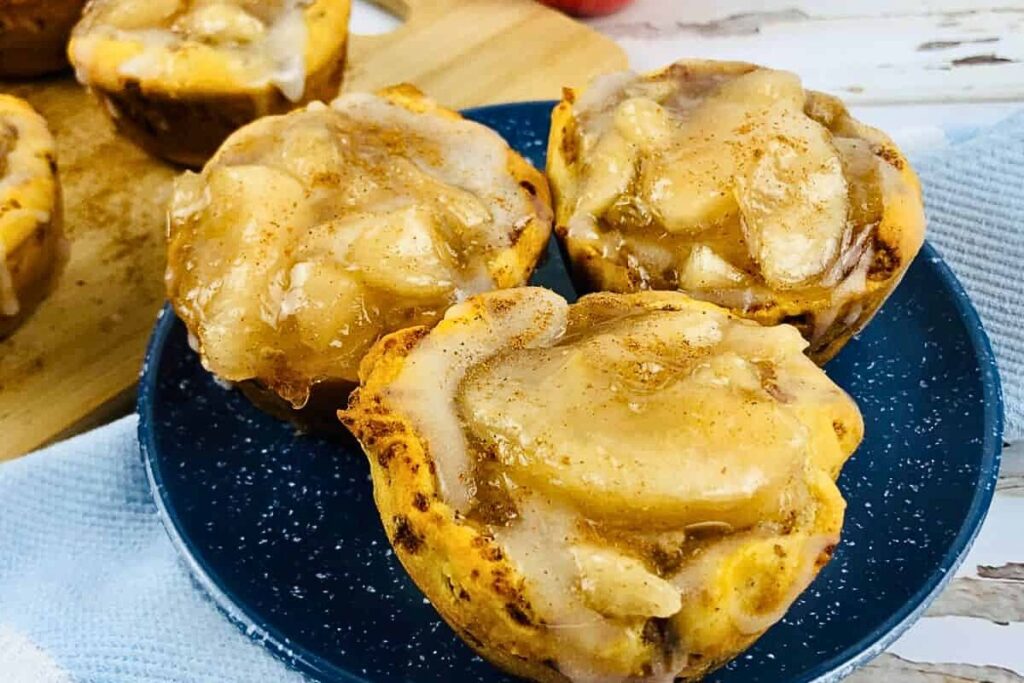 Three cinnamon roll apple pie cups on a plate. 