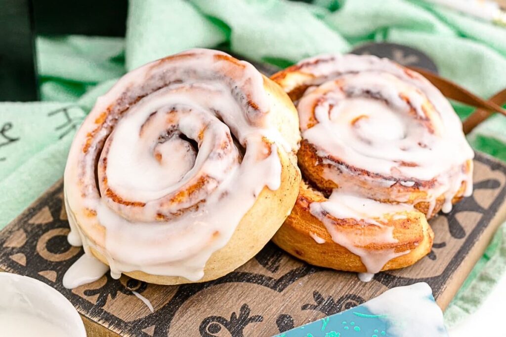 Two cinnamon rolls on a board with frosting.