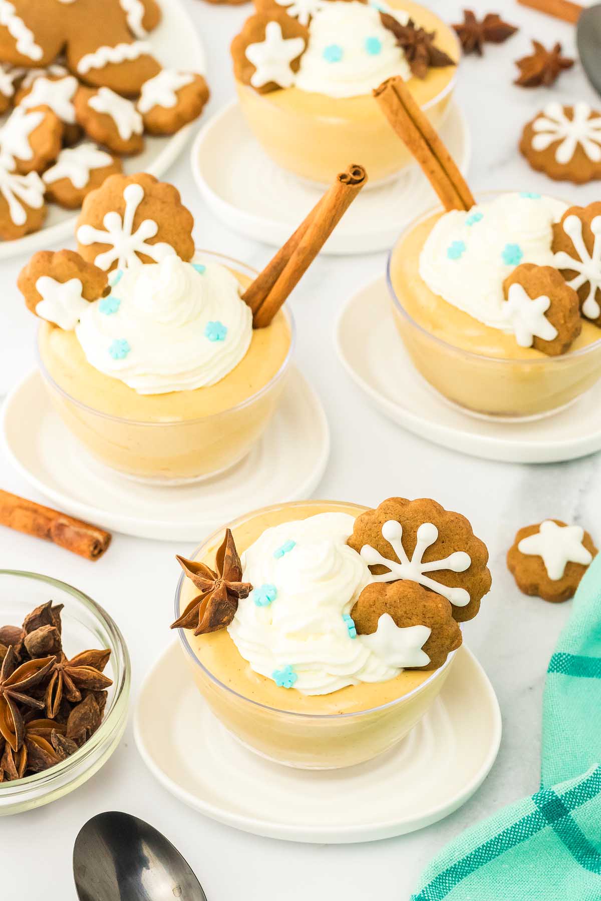 Pumpkin mousse in cups, reminiscent of gingerbread cheesecake jars, topped with whipped cream, gingerbread cookies, and cinnamon sticks, on a white table.