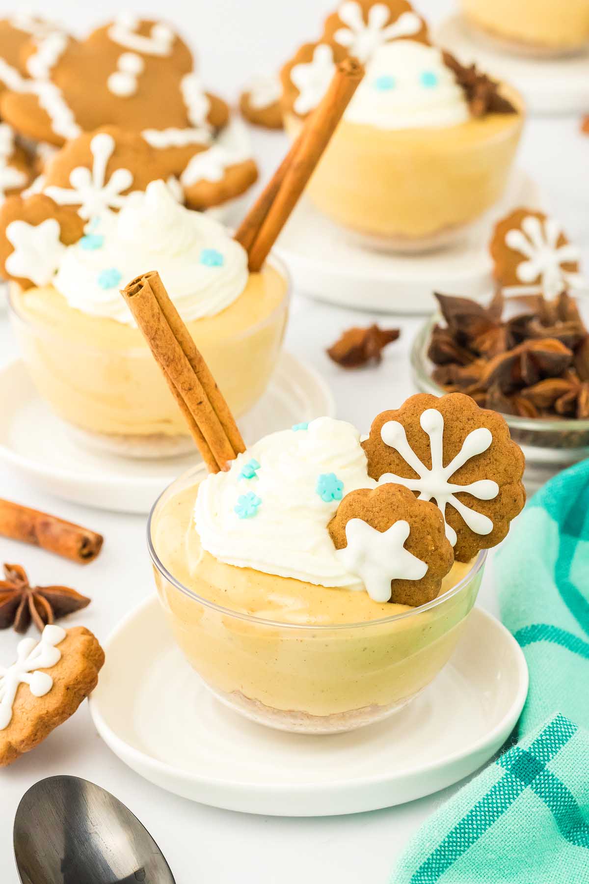 A glass bowl of creamy gingerbread cheesecake jars dessert, topped with whipped cream, a gingerbread cookie, and a cinnamon stick.