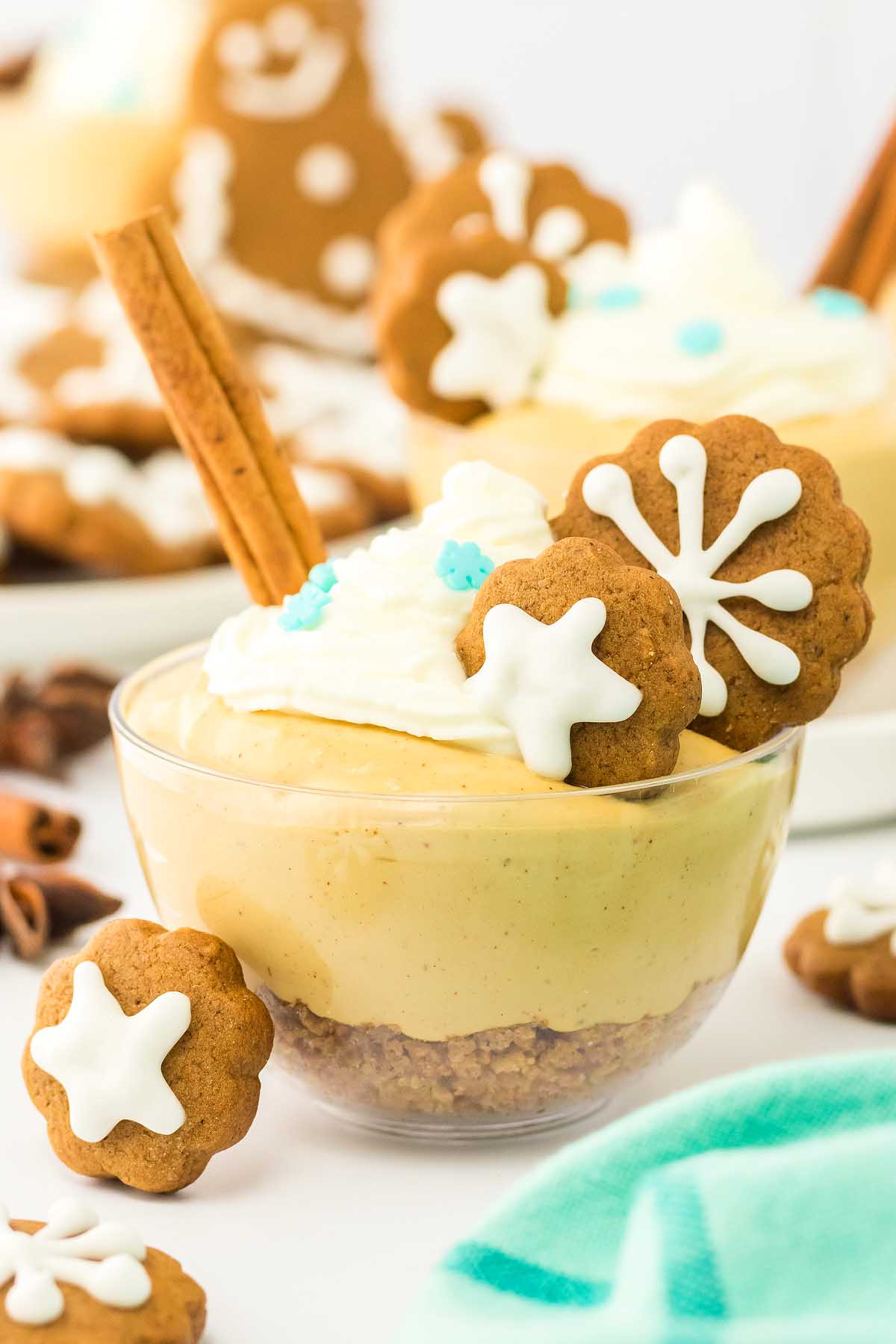 A glass bowl of creamy dessert with whipped topping, gingerbread cookies, and a cinnamon stick as garnish—perfect for fans of gingerbread cheesecake jars.
