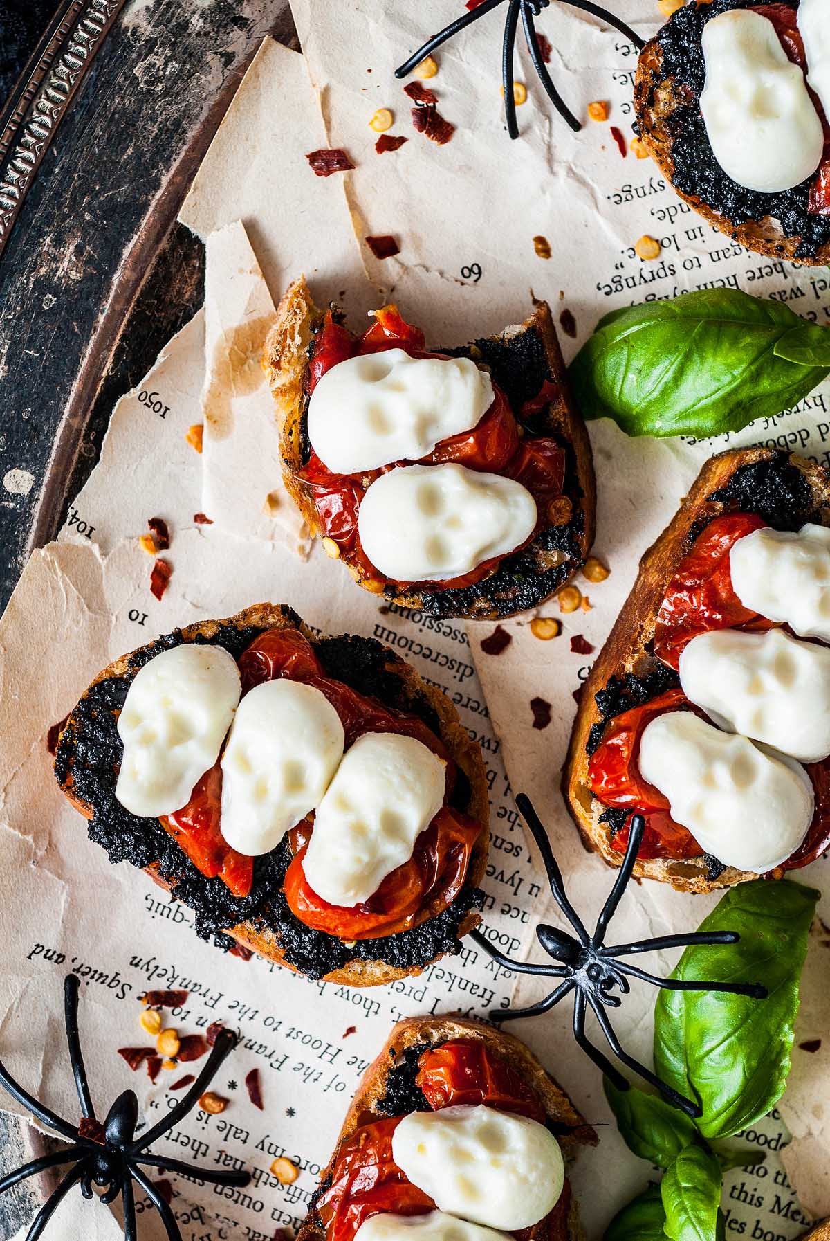 Toasted bread with roasted tomatoes and melted cheese, styled with fake spiders for a spooky Halloween bruschetta appetizer.