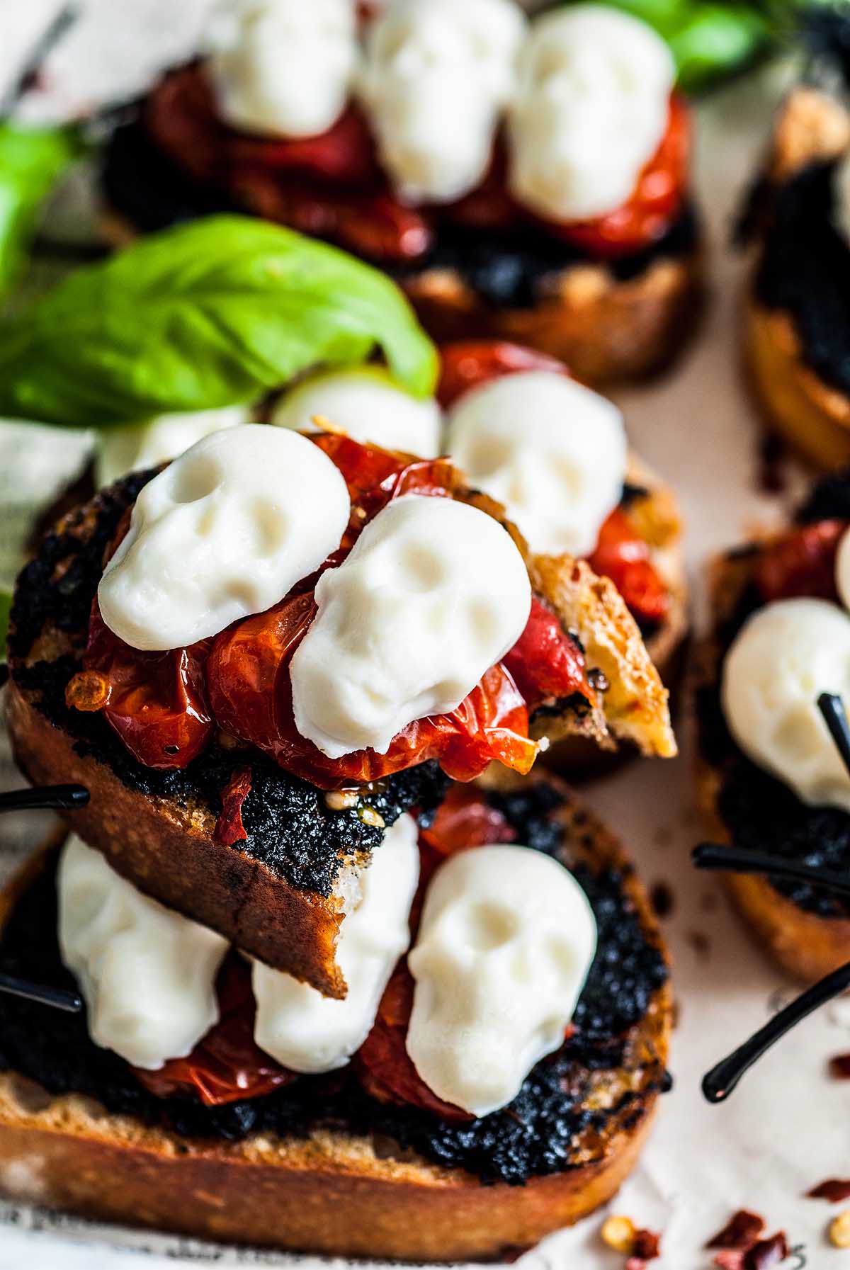 Toasted bread topped with roasted tomatoes and white skull-shaped cheese, garnished with basil—a spooky Halloween bruschetta appetizer perfect for your next Halloween gathering.
