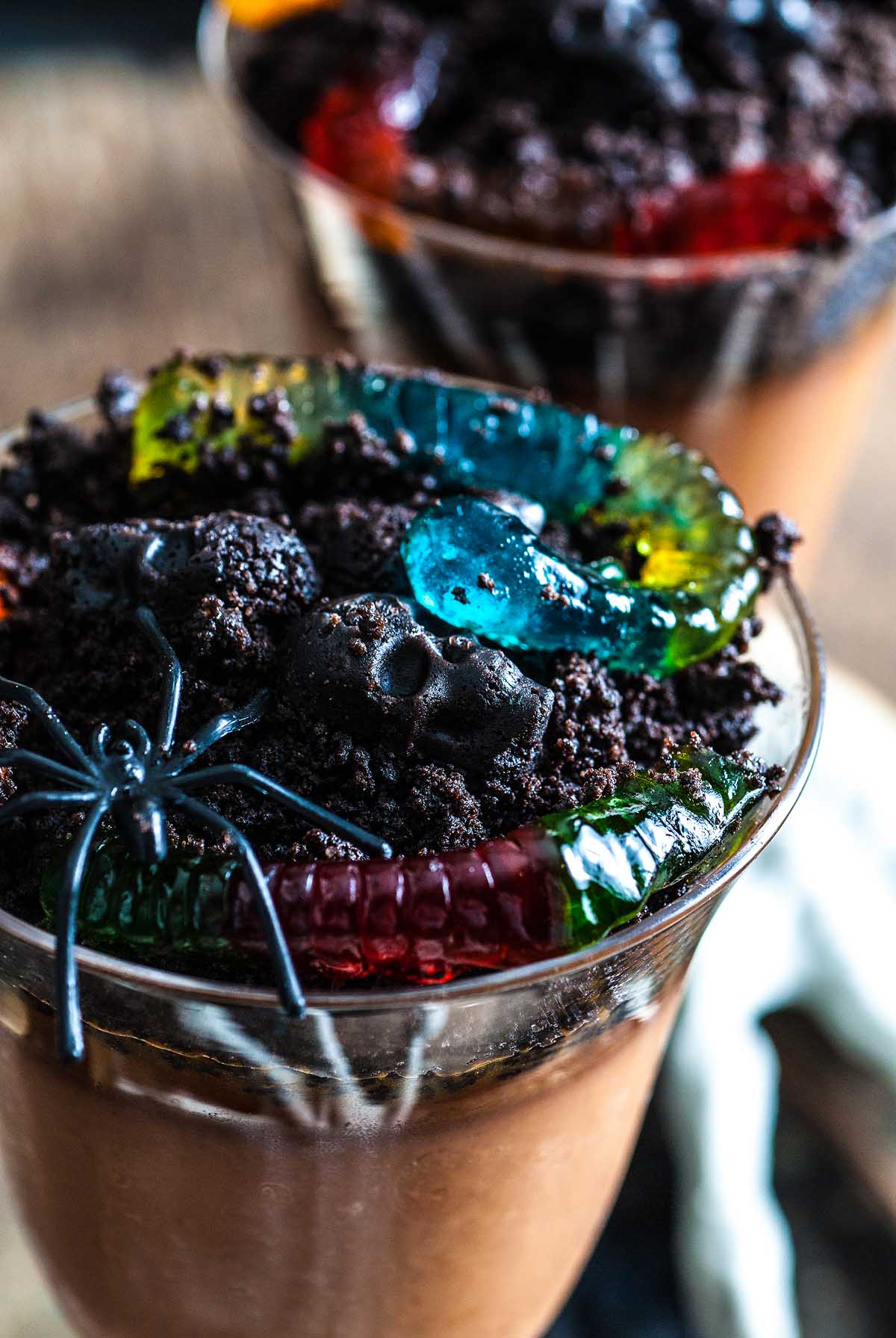 A cup of chocolate pudding topped with crushed cookies, gummy worms, and a plastic spider—this Halloween dessert is a spooky treat everyone will love.